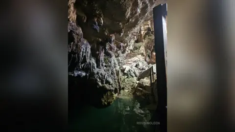RossiNoleen poses inside a dark, rocky cave overlooking a small pool of green water.