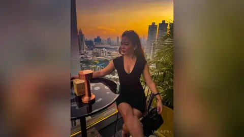 Elegant woman in a black dress enjoying a sunset view on a luxury city rooftop balcony.