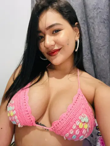 Smiling young woman in a pink crochet bikini top posing indoors with a relaxed mood.