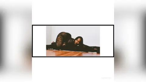 Curvy woman in black lace bodysuit posing on a dark floor in a minimalist white room with a moody vibe.