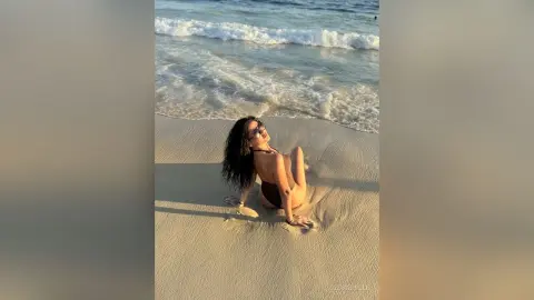 Smiling woman in a dark bikini relaxing on a sunny sandy beach by the ocean waves.