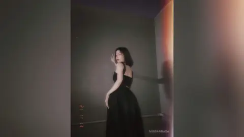 Elegant woman in a black evening gown posing in a moody, dimly lit room.
