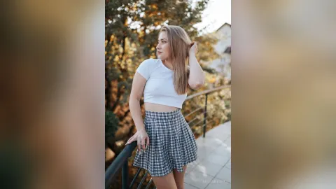 MishaNight — MishaNight stands on a balcony wearing a white crop top and a blue plaid skirt.