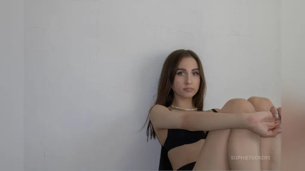 Young woman in black lingerie and high boots posing confidently against a red metallic heart backdrop.