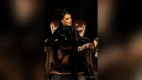 Glamorous woman in a chic black leather outfit sitting on a vintage gold armchair in a moody, dark setting.