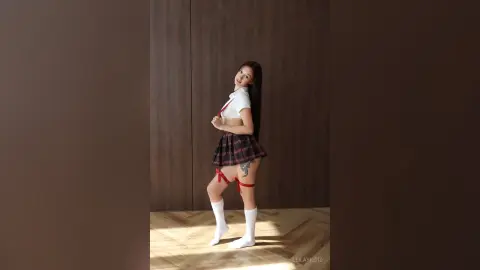 Smiling young woman in a schoolgirl outfit with a plaid skirt posing in a modern minimalist room.