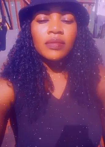 Smiling Black woman in a black tank top and bucket hat enjoying a sunny day outdoors.