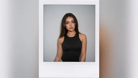 Young woman in a black sleeveless top posing for a moody Polaroid portrait against a grey background.
