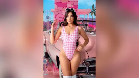 Beautiful woman in pink Barbie swimsuit posing by a vintage pink car in a dreamy pastel summer setting.
