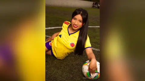 NairaWestbrook wearing a yellow soccer jersey and blue shorts, posing on a grass field while holding a soccer ball.