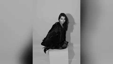 Elegant woman in a flowing black dress posing against a minimalist studio background in a moody black and white portrait.