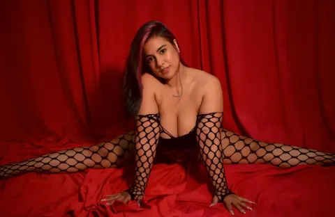 Young woman in black fishnet bodysuit posing against red curtains in a moody, glamorous setting.