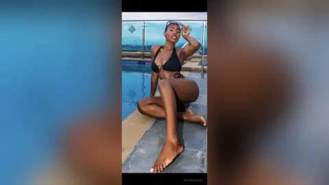 Confident Black woman in a black bikini relaxing by a luxury rooftop swimming pool on a sunny day.