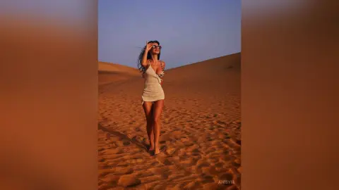 Stylish woman in a white mini dress posing in a vast desert landscape during a golden sunset.