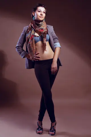 Stylish woman in a blazer, patterned scarf, and black leggings posing confidently against a studio background.