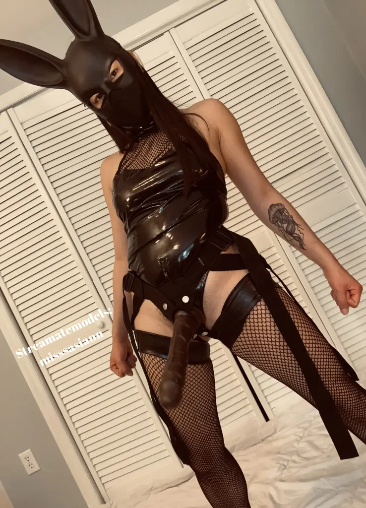 Misssasiann winks while wearing a black face mask and a green lace bra, showing her long dark hair and shoulders.