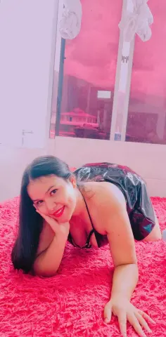 Smiling woman in a black sequin dress relaxing on a pink shaggy rug in a bright room.