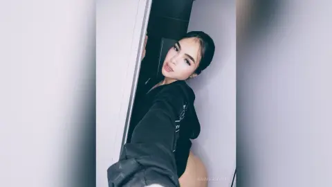 KimmieBloomie poses in a black hoodie, looking over her shoulder with her dark hair pulled back.