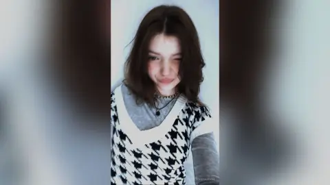 Smiling young woman in a black and white houndstooth sweater posing in a bright indoor setting.