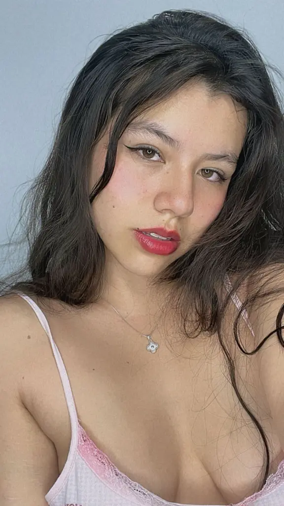 SkyValentiinee poses with a large bouquet of red roses against a spotlight background, looking at the camera with red lipstick.