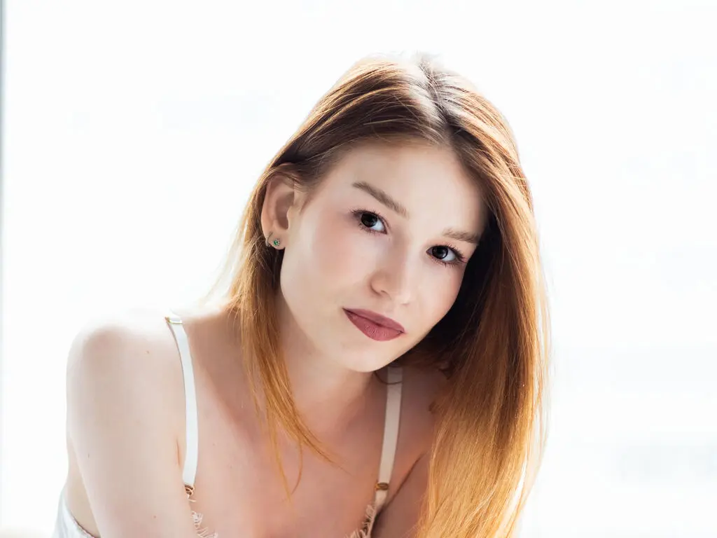 Portrait of a young woman with long brown hair wearing a white camisole in a bright, airy setting.