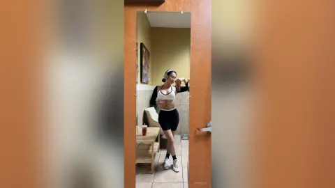 Athletic woman in black yoga shorts and white sports bra posing confidently in a mirror reflection.