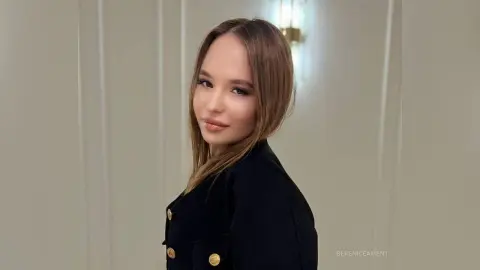 Smiling young woman in a stylish black blazer posing against a neutral indoor background.