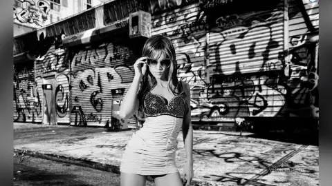 Stylish woman in a tight mini dress posing against a gritty urban graffiti wall in black and white.