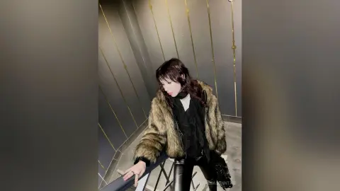 Stylish woman in a cozy brown faux fur jacket and black outfit posing in a modern luxury interior.