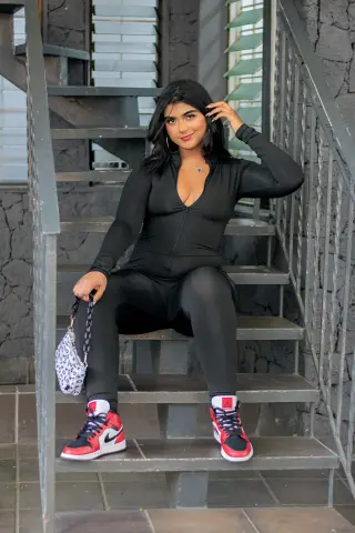 Smiling woman in black athletic outfit and red sneakers sitting on outdoor stairs in a relaxed mood.