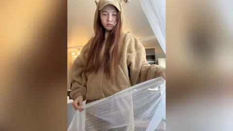 Young woman in a cozy brown fleece hooded romper relaxing indoors with a soft, comfortable aesthetic.