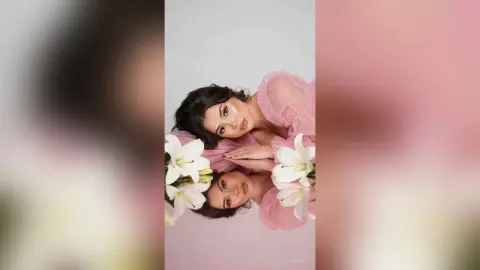 Elegant woman in a pink ruffled blouse posing with white lilies in a soft, romantic studio setting.
