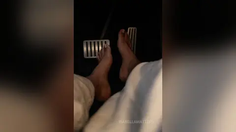 Close-up of bare feet resting on white bedding in a dimly lit, cozy bedroom setting.