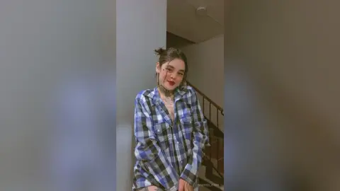 Young woman in a blue plaid flannel shirt posing in a modern indoor hallway with a casual mood.