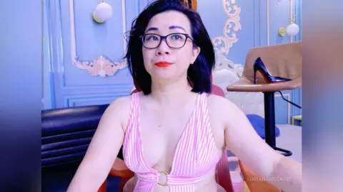 Woman in pink striped swimsuit and glasses sitting in a bright blue room with elegant decor.