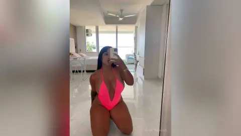 Young woman in a bright pink bikini taking a mirror selfie in a bright, modern minimalist bedroom.