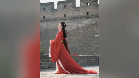 Elegant woman in flowing red Hanfu traditional dress standing by the historic Great Wall of China.