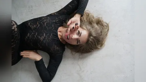Young woman in a black lace bodysuit lying on a light floor with a moody, artistic aesthetic.