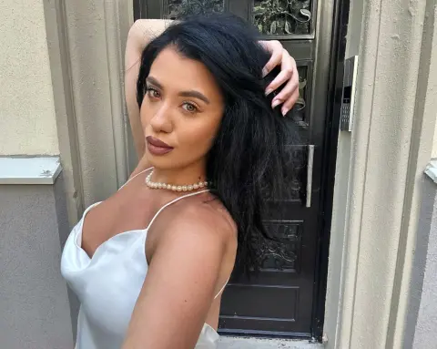 Young woman in a white satin slip dress posing elegantly in front of a black door.