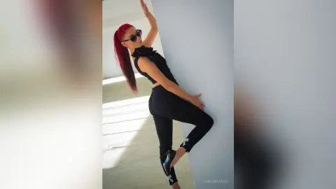 Stylish woman in black sleeveless top and leggings posing confidently in a bright minimalist room.