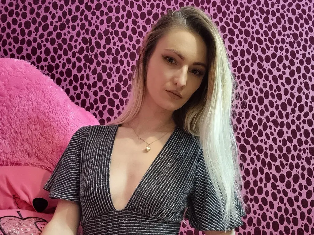 Blonde woman in a sparkly silver V-neck dress sitting against a pink leopard print background.