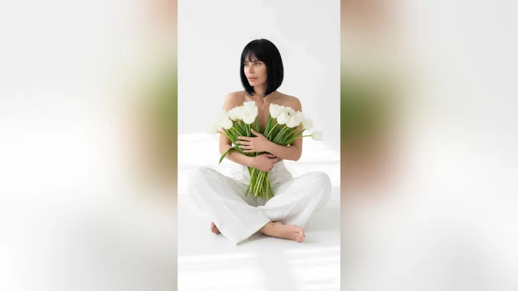 SandraBex — Serene woman with black bob hair in white linen pants holding a bouquet of white tulips in a bright minimalist room.
