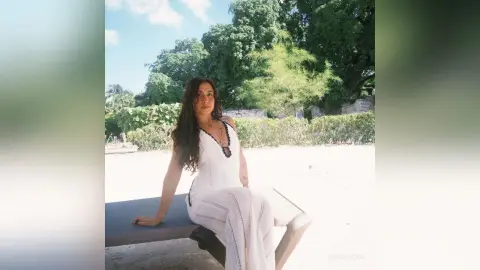 RossiNoleen sits on a lounge chair outdoors wearing a white lace tank top and matching white lace pants.