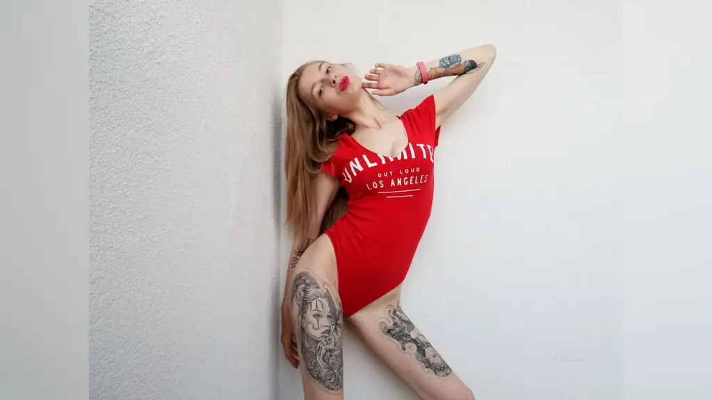 CamilaRomano — Tattooed woman in a red Los Angeles graphic bodysuit posing confidently against a white wall.