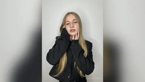 Blonde woman in a chic black blazer posing against a white background with a soft, elegant mood.