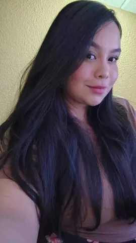 Smiling woman with long dark hair wearing a casual brown top in a warm indoor setting.