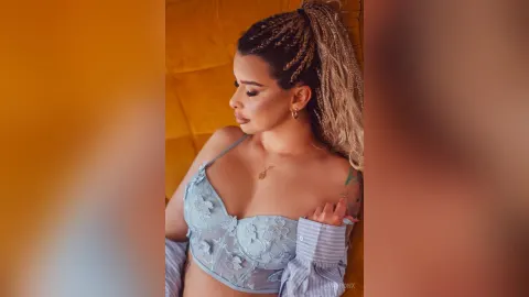 AvaBronX — AvaBronX wears a light blue lace bra while posing against a yellow background.