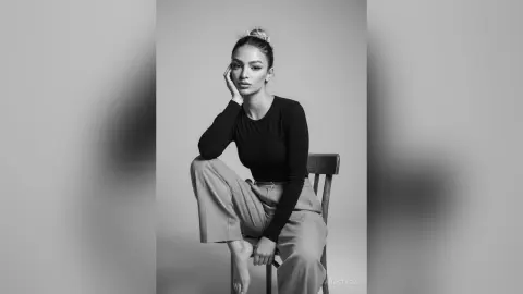 Elegant woman in black long-sleeve top and trousers posing thoughtfully in a minimalist studio setting.