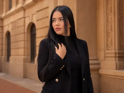 Elegant woman in a black blazer and turtleneck posing against a classic beige stone building architecture.