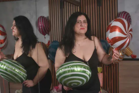 Woman in a black dress holding festive red and white striped balloons in a modern room.